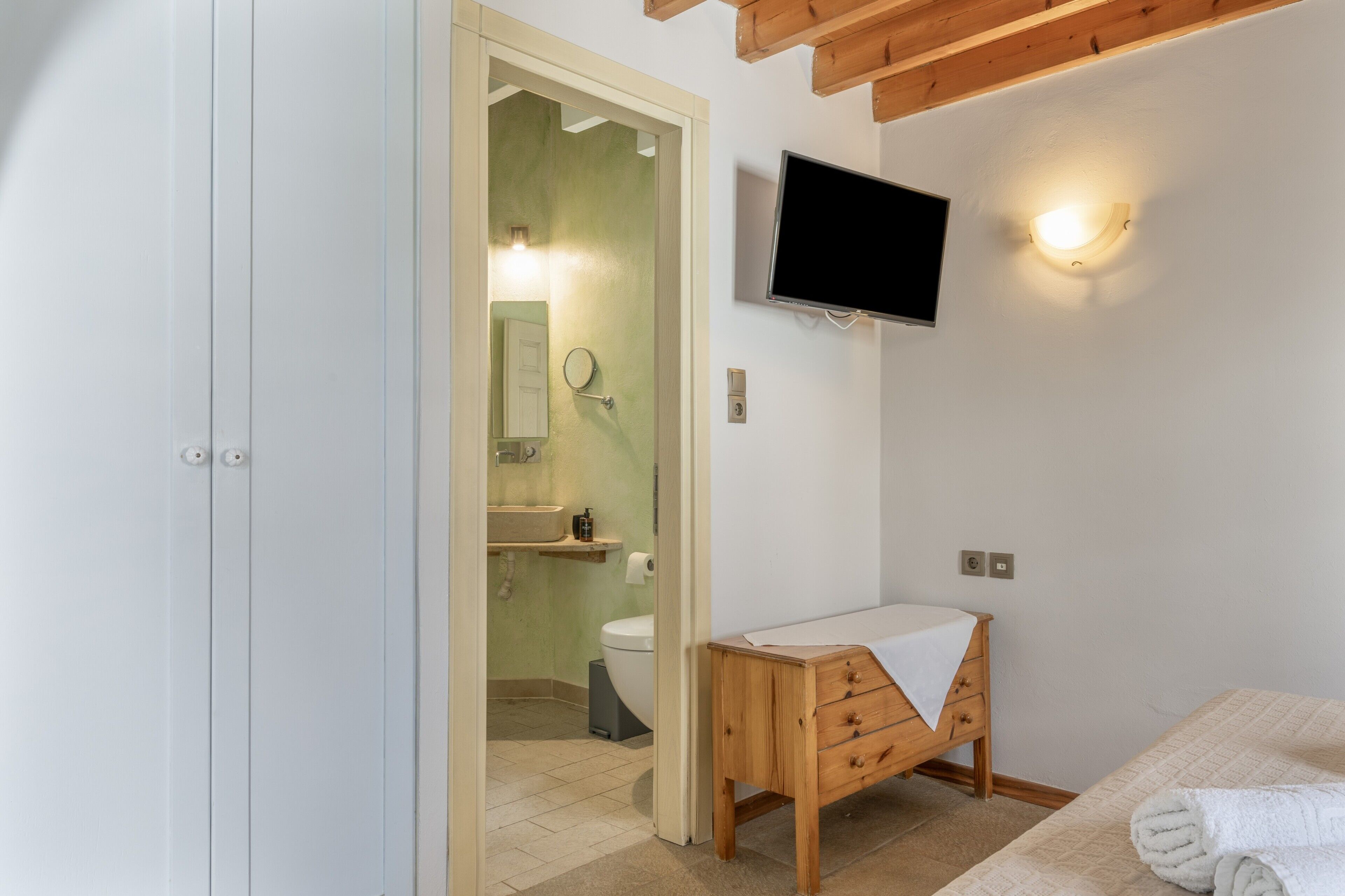 Un baño con inodoro, lavabo, espejo y televisor montado en la pared.