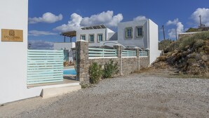 A white building with a sign reading 'SANTANA SUITES,' a stone wall, and a gravel driveway. - Room 'Triple  Pool View No 2' with Shared Pool, Wi-Fi and Air Conditioning (Patmos)