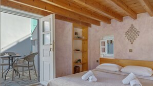 Une chambre avec un plafond en bois, un lit recouvert de draps blancs, une petite table avec des chaises et une fenêtre.