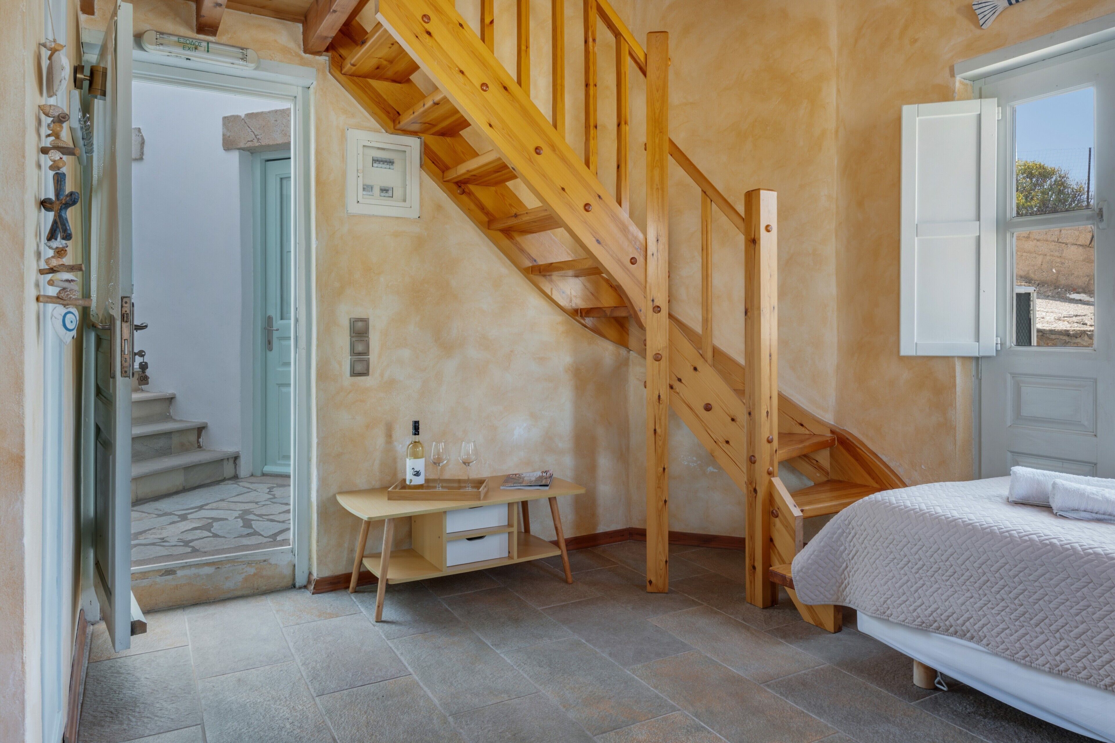 Ein Schlafzimmer mit einer Holztreppe, einem Bett, einem Nachttisch mit Flasche und Gläsern sowie einem Fenster mit Blick.
