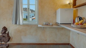 Une cuisine équipée d’un réfrigérateur, une fenêtre donnant sur des immeubles, un plateau avec des tasses et un panier de fruits.