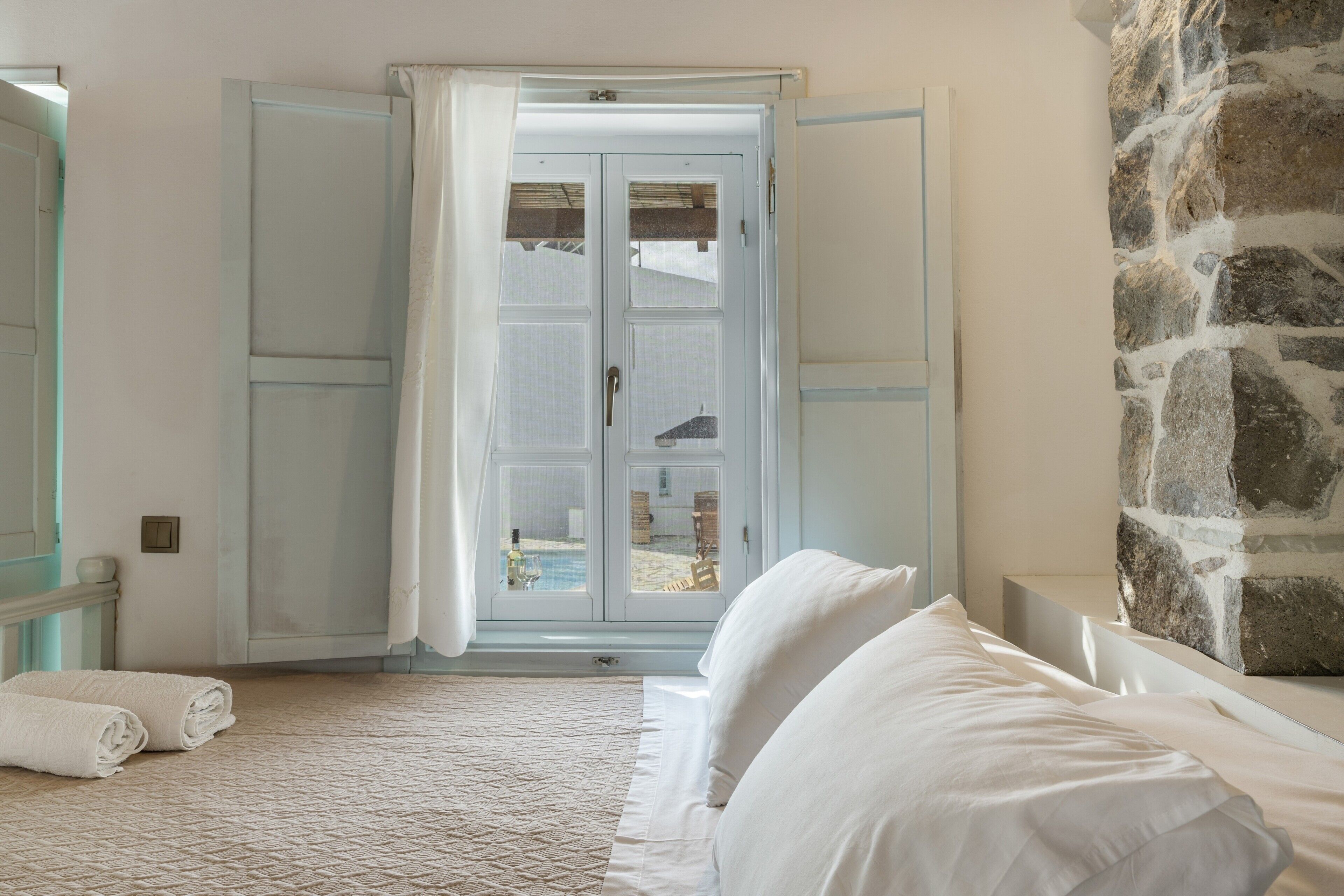 Une chambre à coucher avec un lit, un mur en pierre et une porte donnant sur un balcon.