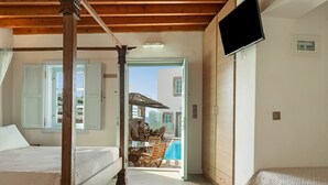 A bedroom with a wooden ceiling, a TV mounted on the wall, and a view of an outdoor swimming pool area.