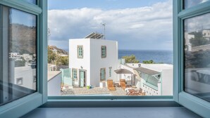 Blick durch ein Fenster auf ein weißes Gebäude mit Balkon, Außenbereich und Meerblick.