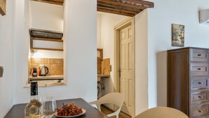 A dining area with a wooden table, white chairs, a wine bottle, and a plate of grapes.
