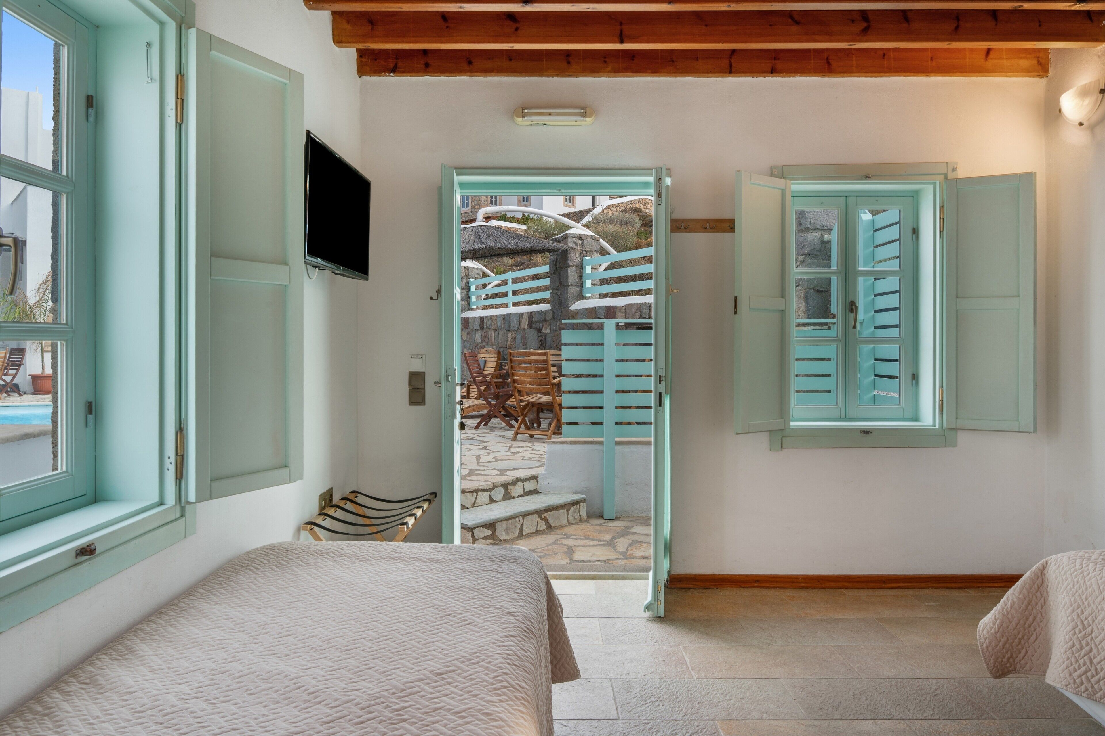 Une chambre avec un lit, une télévision et une vue sur un patio extérieur doté d’un mur en pierre et de meubles en bois.