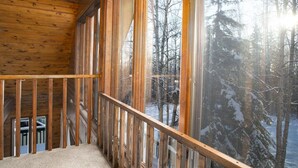 A wooden cabin with a balcony overlooking a snowy forest.