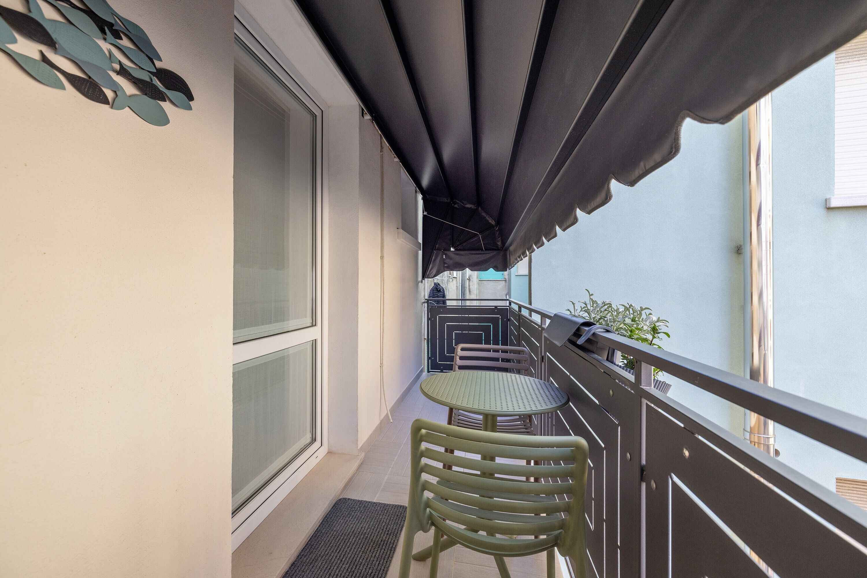 Un balcone con tavolo e sedie, una finestra e un tendaggio scuro.