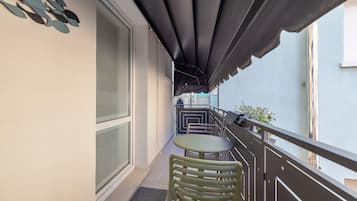 Un balcone con tavolo e sedie, una finestra e un tendaggio scuro.