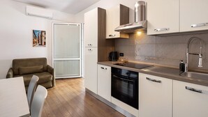 A modern kitchen with a built-in oven, a stainless steel sink, and a dining area with a table and chairs. - Apartment 'Appartamento Bettin' with Private Terrace, Wi-Fi and Air Conditioning (Caorle)