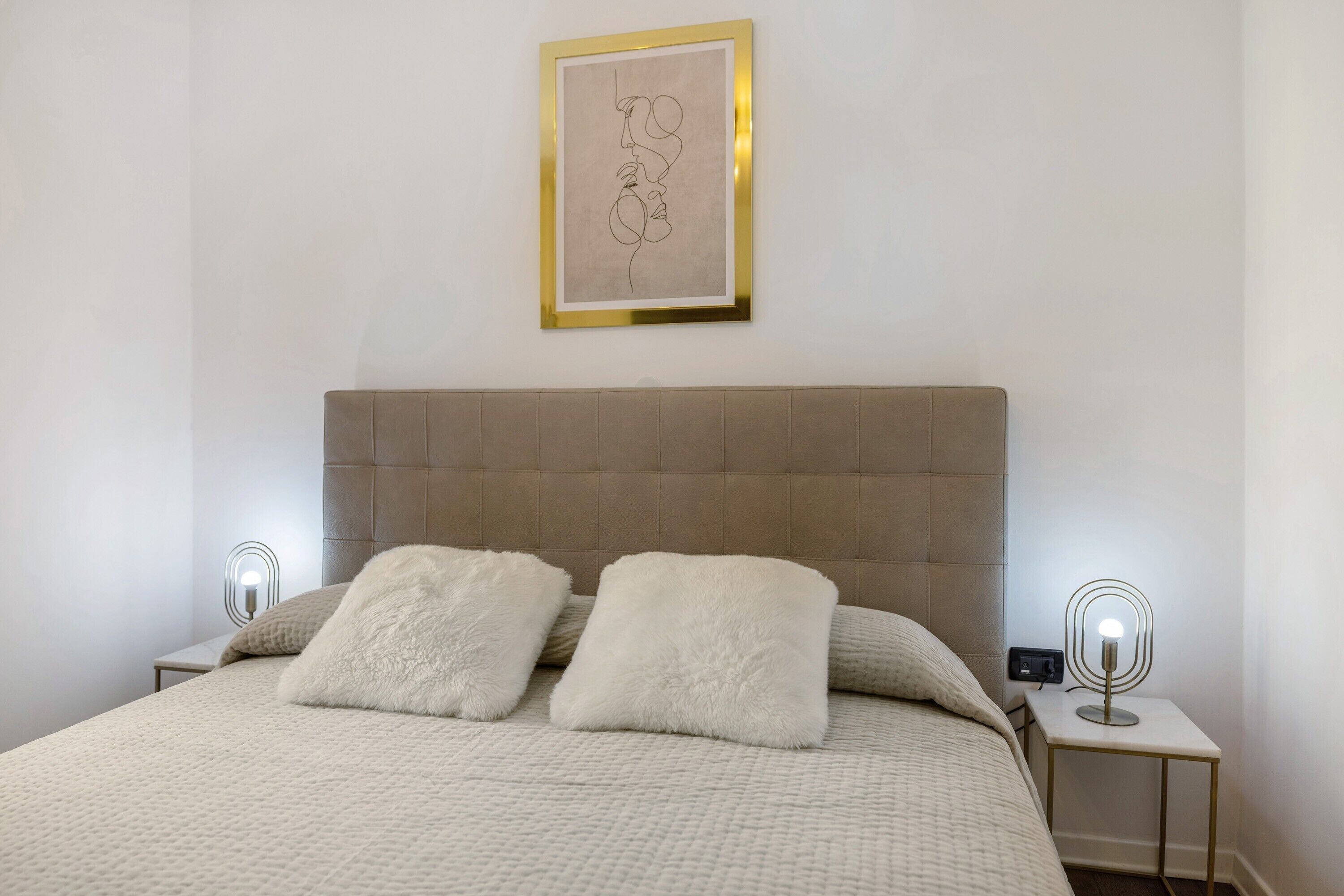 Una camera da letto con un letto, due cuscini soffici, una testiera, un comodino con una lampada e un'opera d'arte incorniciata al muro.