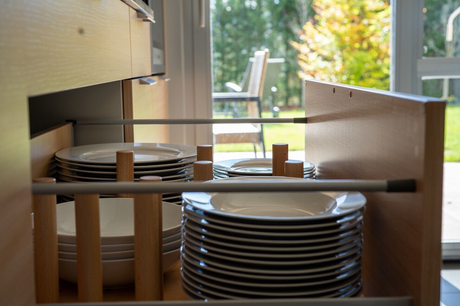 A stack of plates in a wooden cabinet with a view of a garden outside.