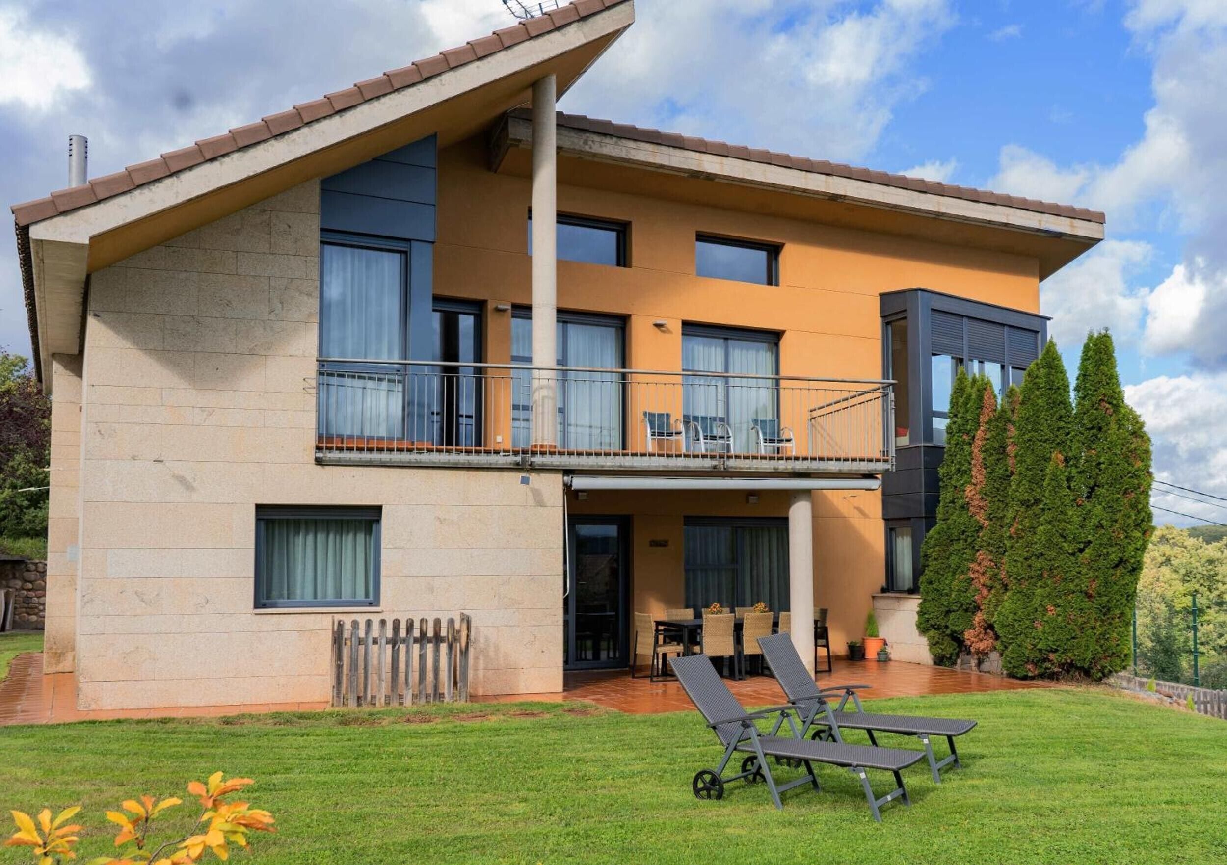 Une maison à deux étages dotée d’un balcon, d’une terrasse avec des meubles d’extérieur et d’une pelouse bien entretenue.
