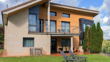 Une maison à deux étages dotée d’un balcon, d’une terrasse avec des meubles d’extérieur et d’une pelouse bien entretenue.