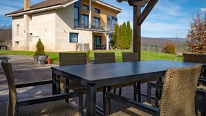 A covered outdoor dining area with a table and chairs, a stone building with a balcony in the background, and a clear sky. - Villa 'Casa El Rasillo' with Lake View, Private Terrace and Wi-Fi (El Rasillo de Cameros)