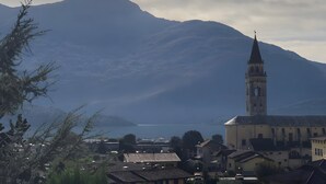 Une ville qui se distingue par son imposant clocher, ses maisons aux toits de tuiles et une montagne qui se profile à l’arrière-plan.