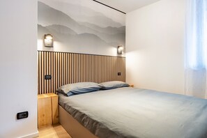Une chambre moderne avec un lit, une tête de lit en bois, des lampes fixées au mur et une fresque représentant une montagne.