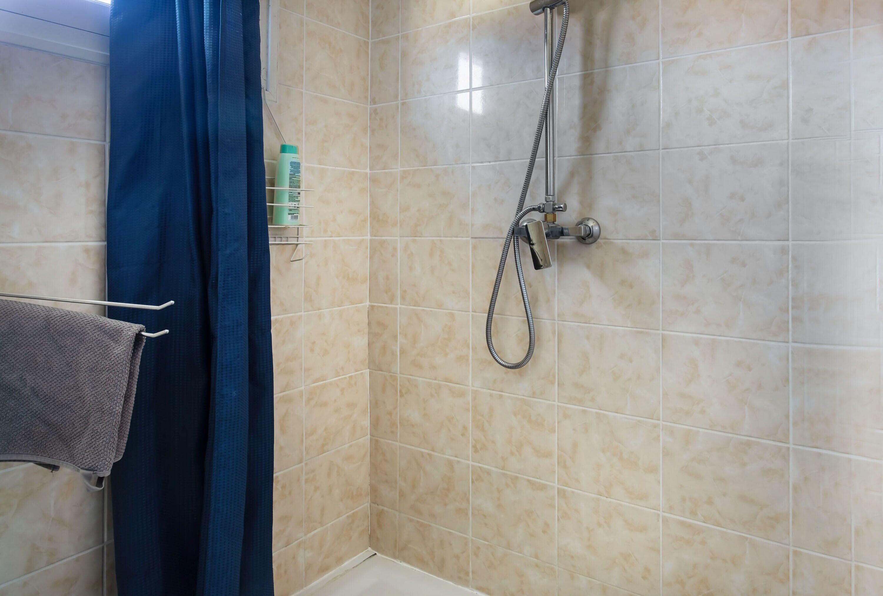 Une salle de bain avec des carreaux de couleur beige, une pomme de douche et un porte-serviettes sur lequel est posée une serviette.