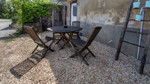 Une terrasse avec une table ronde et quatre chaises, un banc en bois, une échelle en métal et un petit espace jardin agrémenté d’une plante et d’une clôture en bois.