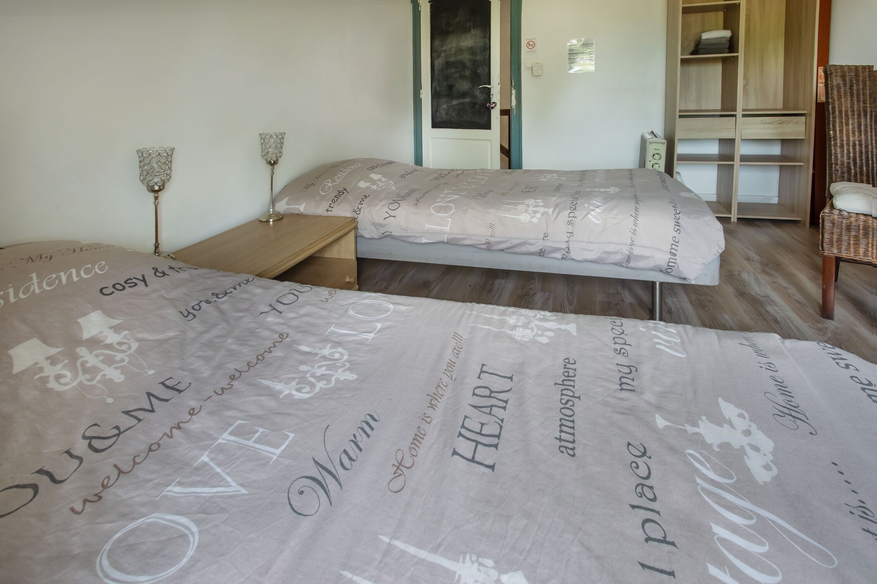 Een slaapkamer met twee bedden, een houten nachtkastje, een rieten stoel en een garderobe.