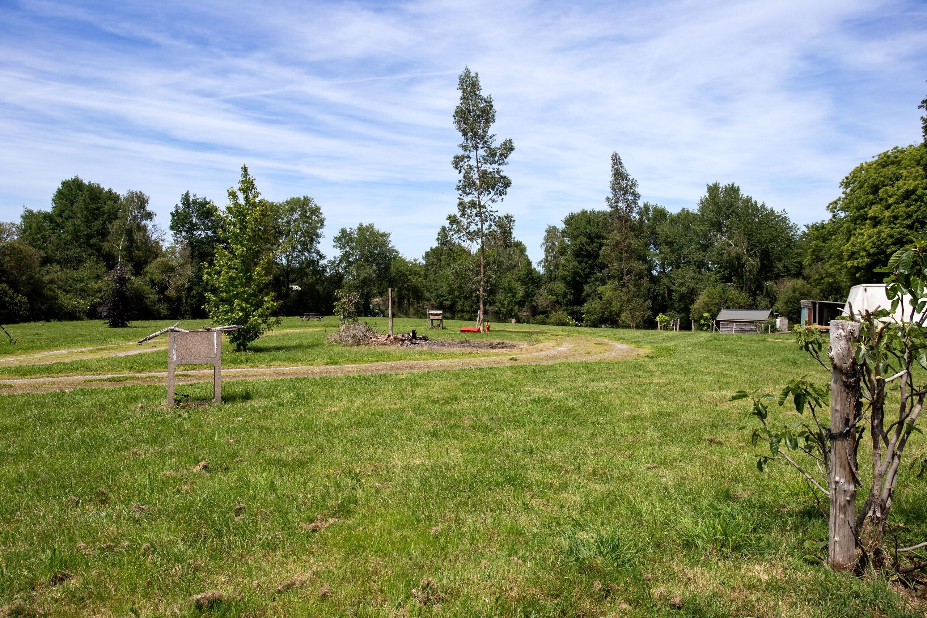 Eine grüne Wiese mit einer Holzhütte, Bäumen und blauem Himmel.