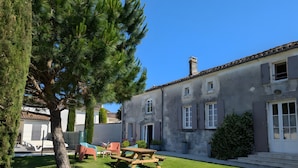 A building with a rustic exterior, a wooden picnic table, and a large tree in the foreground. - Holiday Home 'La Bonne Chauffe' with Shared Pool, Private Terrace and Wi-Fi (Verrières)
