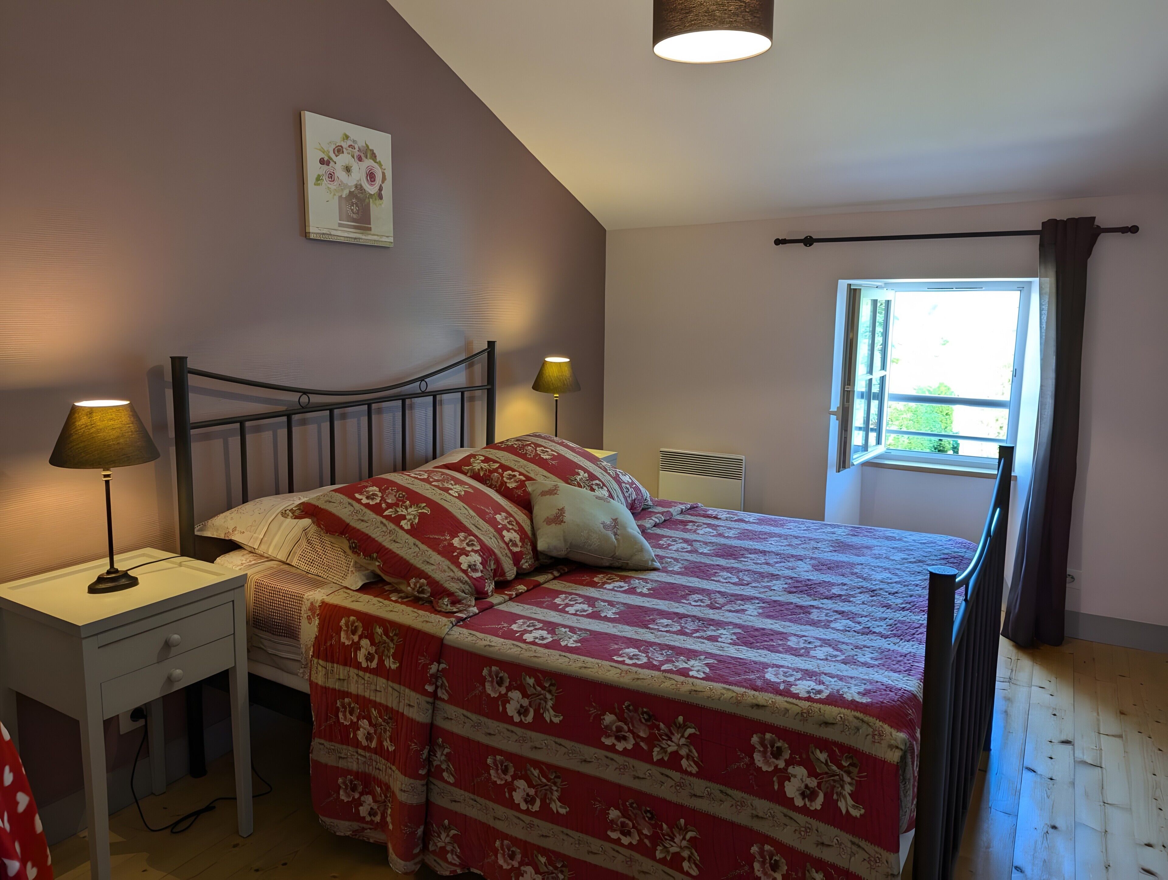 A bedroom with a bed, bedside tables, a window, and a wall-mounted picture.