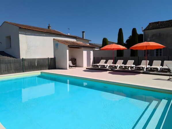 A swimming pool with lounge chairs and umbrellas, a fenced area, and a building with a tiled roof. - Holiday Home 'La Bonne Chauffe - Serpentin' with Shared Pool, Private Terrace and Wi-Fi (Verrières)