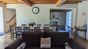 A living room with a dark brown sofa, wooden beams on the ceiling, a dining table with chairs, and a kitchen area in the background. - Holiday Home 'La Bonne Chauffe - Serpentin' with Shared Pool, Private Terrace and Wi-Fi (Verrières)