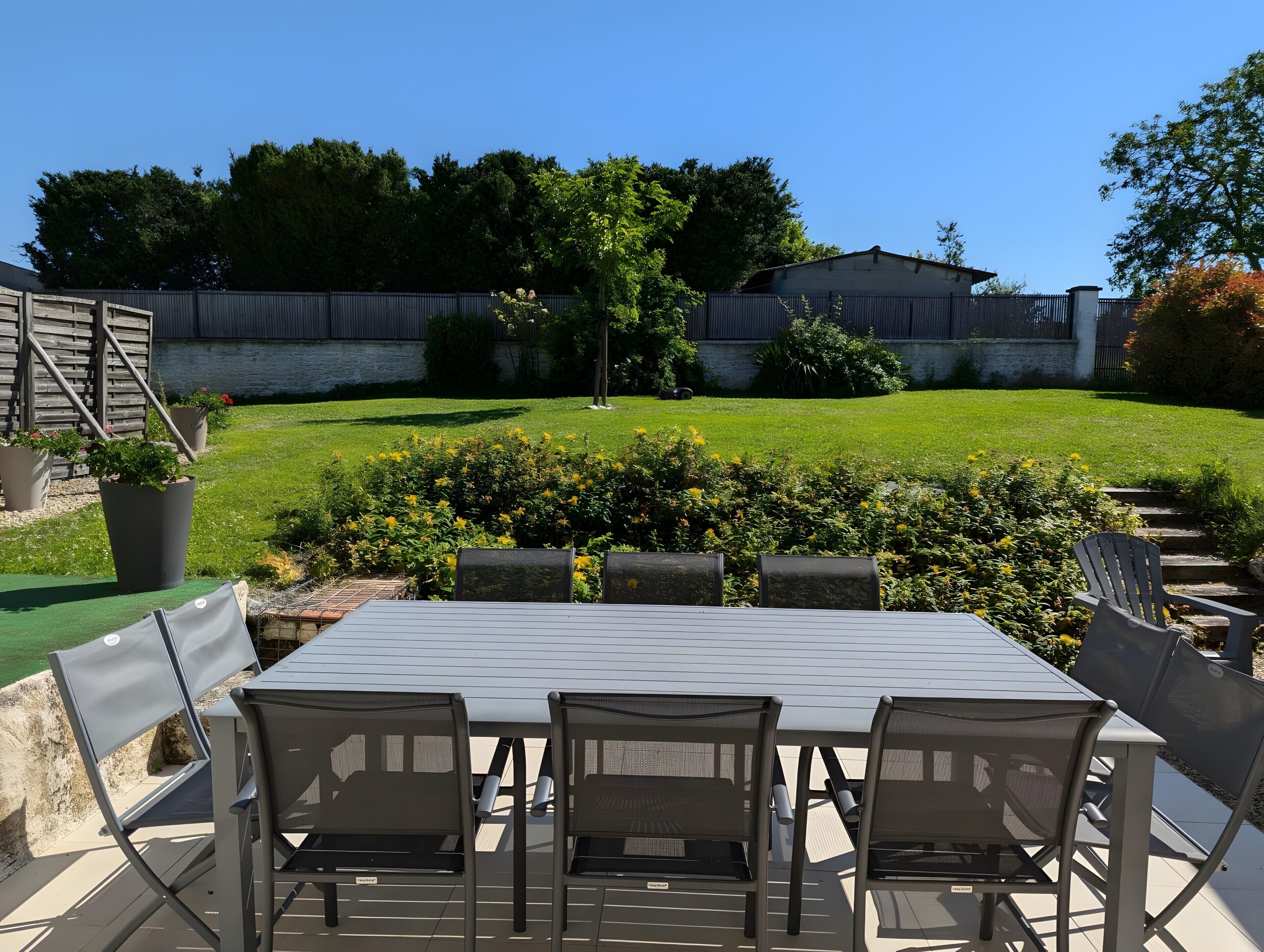 A patio with a table and chairs, surrounded by a well-maintained lawn and a wooden fence.