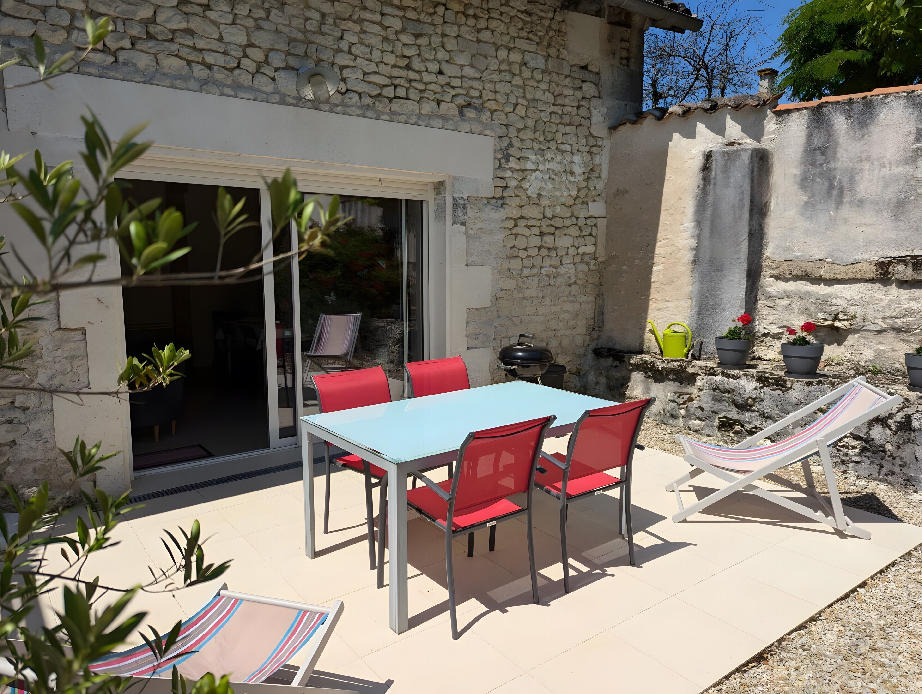 A patio with a table and chairs, a grill, and potted plants.