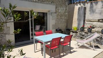 A patio with a table and chairs, a grill, and potted plants.