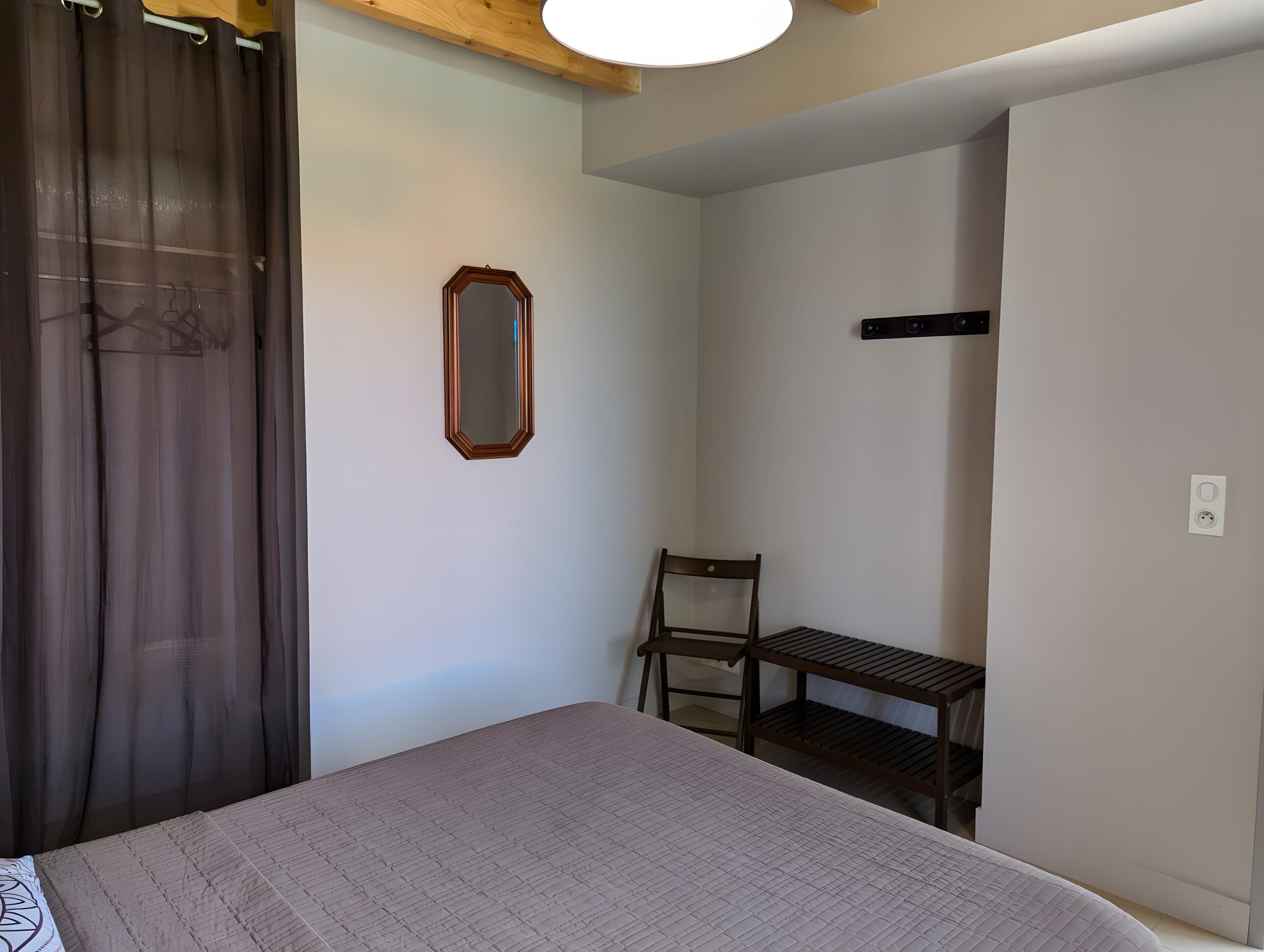 Una camera da letto con un letto, una sedia, un tavolino, uno specchio e una lampada a sospensione.