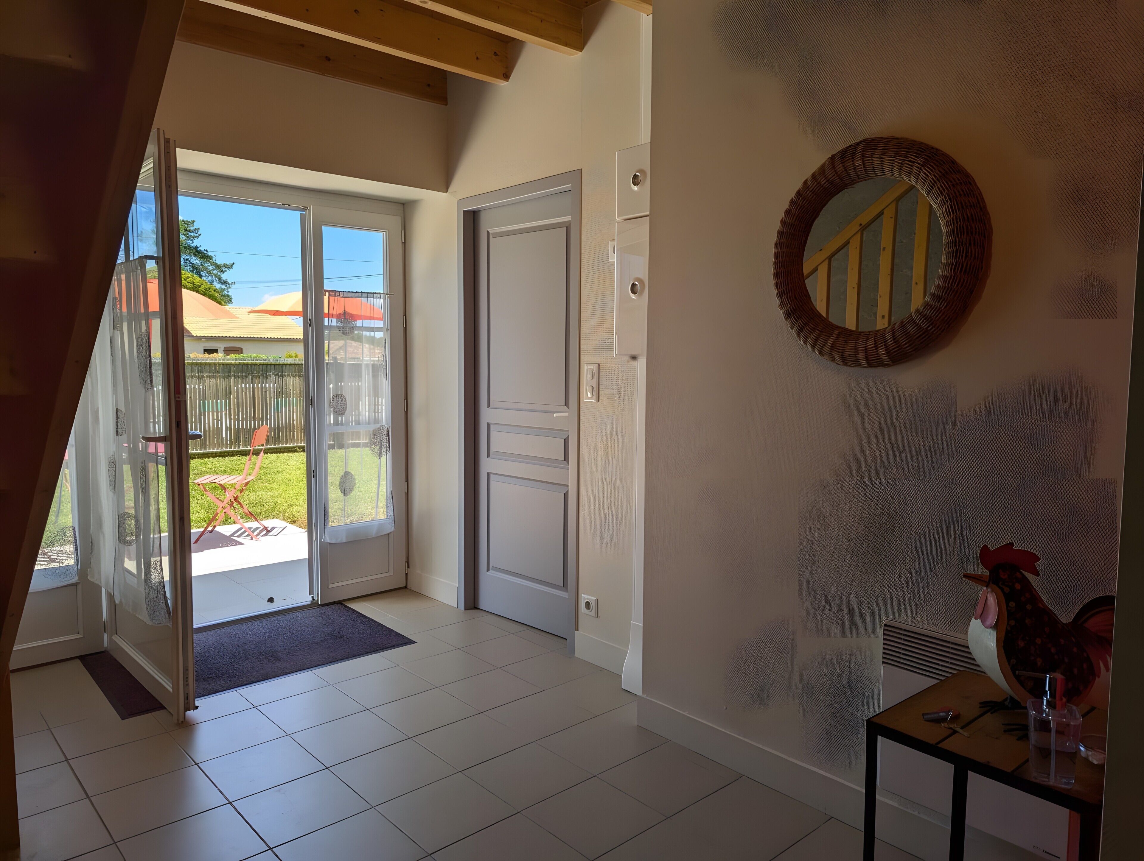 A room with a sliding glass door leading to a patio, a white door, a mirror on the wall, and a small table with a rooster decoration.
