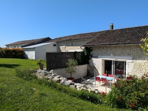 A stone building with a tiled roof, a grassy yard, and a patio with outdoor furniture.