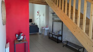 A living room with a wooden staircase, a red wall, a sofa, a table with a rooster decoration, and a floor lamp. - Holiday Home 'La Bonne Chauffe-Col De Cygne' with Shared Pool, Private Terrace and Wi-Fi (Verrières)