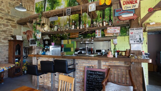 A rustic bar area with wooden shelves, a chalkboard menu, and a stone wall backdrop.