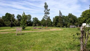A grassy field with a wooden structure, trees, and a clear sky.