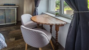 A room with a wooden table, a chair with a polka dot cushion, a metal cabinet, and a window with curtains.
