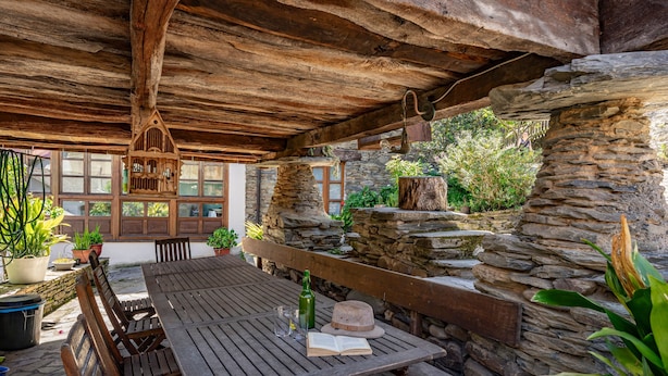 Un espace de restauration extérieur rustique, avec une table en bois, des bancs, des murs en pierre et des lanternes suspendues.