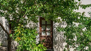 Un bâtiment avec une porte en bois, une fenêtre et un arbre devant.