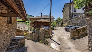 Une ruelle étroite pavée de pierres, bordée d’immeubles en pierre, avec une structure en bois portant une enseigne et des voitures garées.