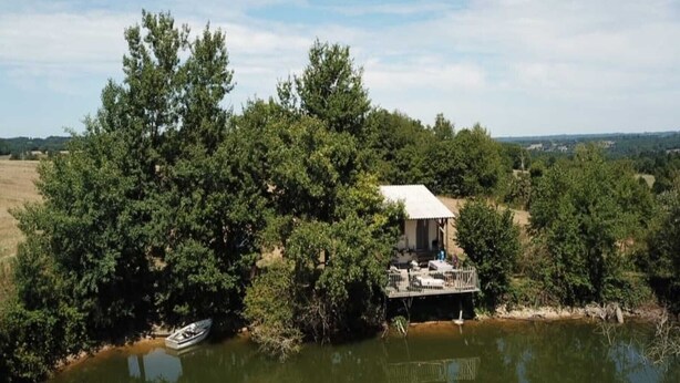 Un chalet au bord du lac, doté d’une terrasse, entouré d’une forêt dense et avec un bateau amarré à proximité.
