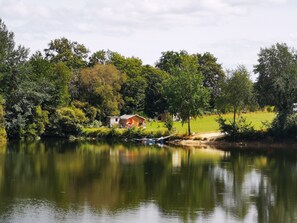 A lakeside cabin with a dock, surrounded by dense trees and a grassy field.