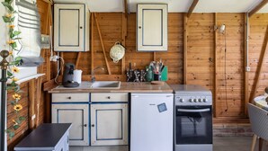 A compact kitchen with wooden walls, a sink, a stove, and a refrigerator. - Chalet by Bramefort Pond (Champsac)