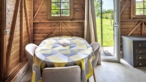 A wooden cabin with a round table, chairs, and a view of the outdoors. - Chalet by Bramefort Pond (Champsac)