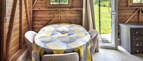 A wooden cabin with a round table, chairs, and a view of the outdoors.