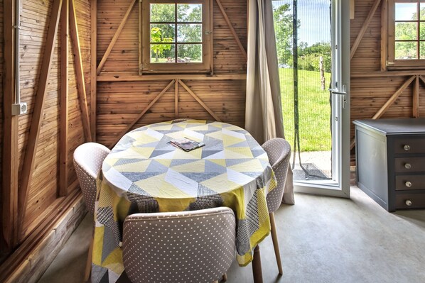 A wooden cabin with a round table, chairs, and a view of the outdoors.