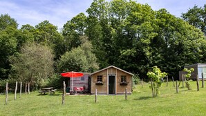 A small wooden cabin with a picnic table and a red umbrella in a grassy area with trees. - Chalet by Bramefort Pond (Champsac)