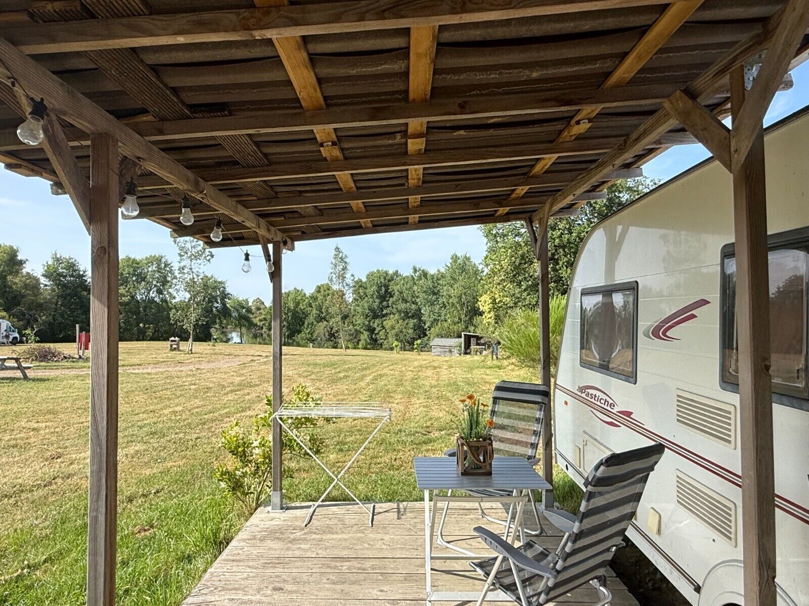 Un espace extérieur abrité, équipé d’une table de pique-nique et de chaises, d’un barbecue, et où un camping-car est stationné à proximité.